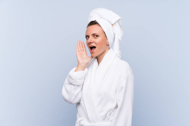 Woman in bathrobe over isolated blue background shouting with mouth wide open - Фото, зображення
