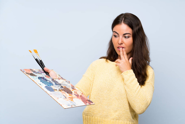 Молодая художница на изолированном синем фоне с удивлением и шокированным выражением лица
 - Фото, изображение