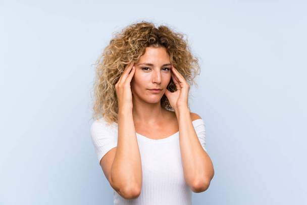 Young blonde woman with curly hair over isolated blue background unhappy and frustrated with something. Negative facial expression - Foto, Bild