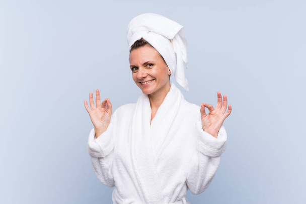 Woman in bathrobe over isolated blue background showing an ok sign with fingers - Photo, Image