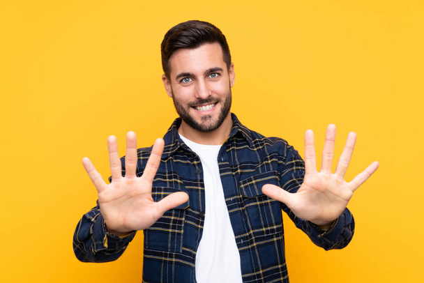 Jonge knappe man met baard over geïsoleerde gele achtergrond tellen tien met vingers - Foto, afbeelding