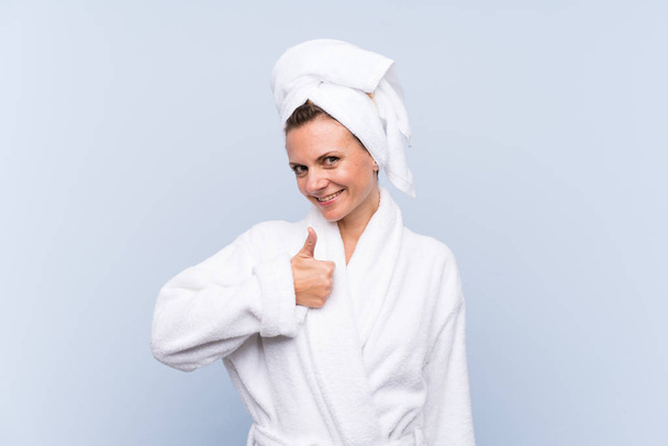 Woman in bathrobe over isolated blue background giving a thumbs up gesture - Фото, зображення