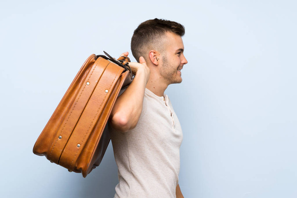 Young handsome blonde man over isolated blue background holding a vintage briefcase - Fotó, kép