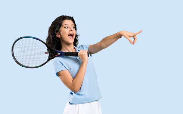 Joven jugadora de tenis sorprendida y señalando con el dedo hacia un lado sobre un fondo aislado
 - Foto, Imagen