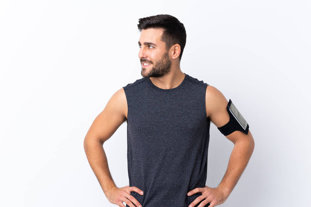 Young sport handsome man with beard over isolated white background posing with arms at hip and looking side - Fotoğraf, Görsel