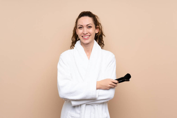 Young woman in a bathrobe holding makeup brushes smiling a lot - Photo, Image