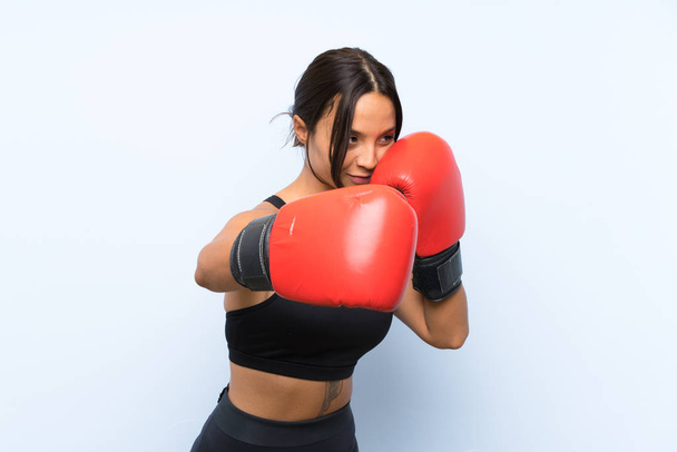 Joven chica deportiva con guantes de boxeo sobre fondo azul aislado
 - Foto, imagen