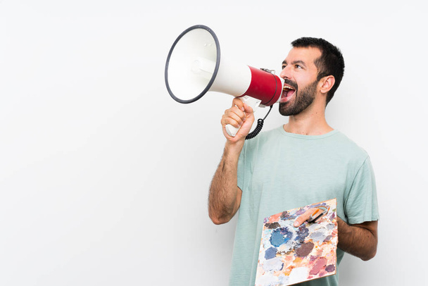 Mladý umělec muž drží paletu přes izolované pozadí křičí přes megafon - Fotografie, Obrázek