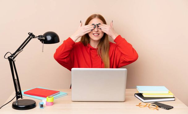 Young student woman in a workplace with a laptop covering eyes by hands - Photo, Image
