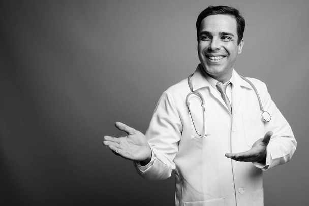 Studio shot of handsome Persian man doctor against gray background in black and white - 写真・画像