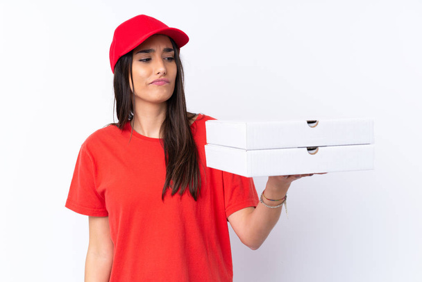 Mujer de entrega de pizza sosteniendo una pizza sobre una pared blanca aislada con expresión triste
 - Foto, imagen