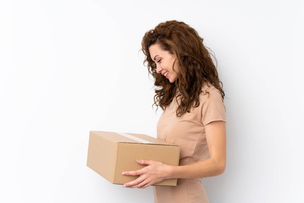Молодая красивая женщина на изолированном фоне держит коробку, чтобы переместить ее на другой сайт
 - Фото, изображение