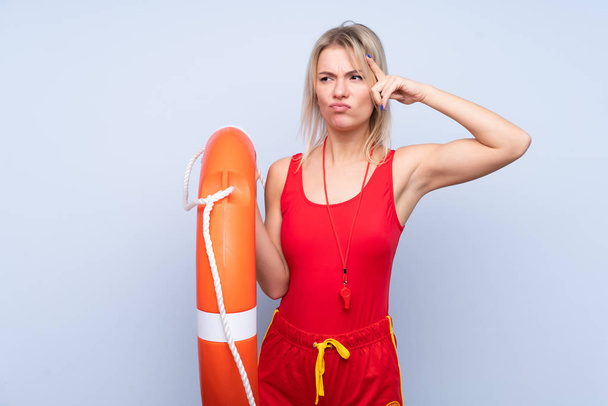 Rettungsschwimmerin vor isoliertem blauen Hintergrund mit Rettungsschwimmerausrüstung und Zweifeln mit verwirrtem Gesichtsausdruck - Foto, Bild