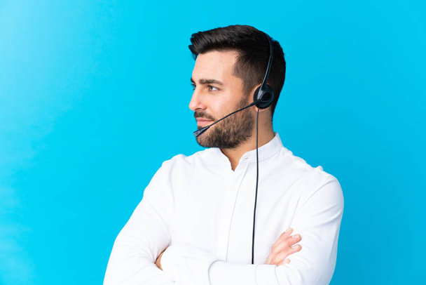 Telemarketer man working with a headset over isolated blue background looking to the side - Photo, Image