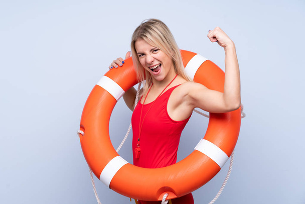 Salva-vidas mulher sobre fundo azul isolado com equipamento salva-vidas e fazendo gesto forte
 - Foto, Imagem