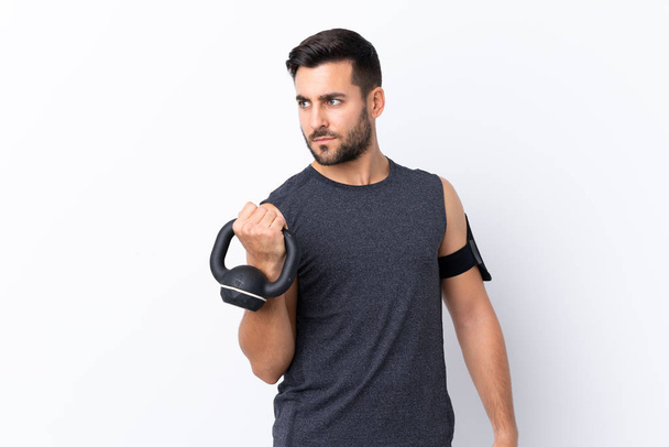 Young sport handsome man with beard over isolated white background making weightlifting with kettlebell - Fotoğraf, Görsel
