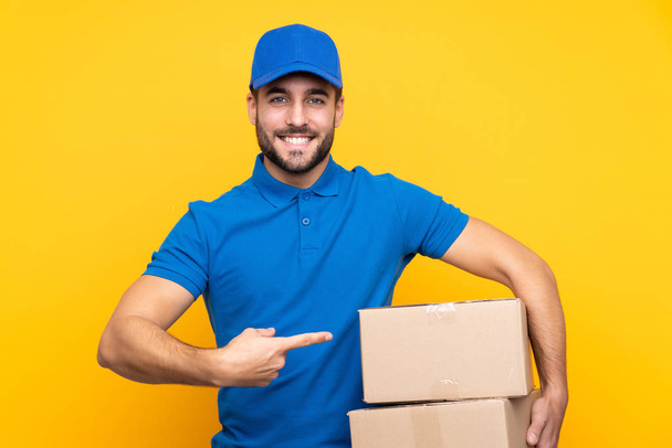 Delivery man over isolated yellow background and pointing it - Photo, Image