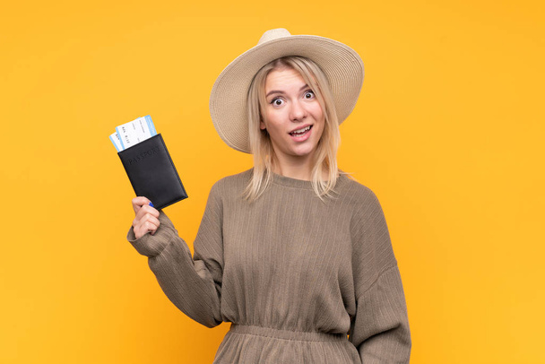 Jonge blonde vrouw over geïsoleerde gele achtergrond gelukkig in vakantie met paspoort en vliegtickets - Foto, afbeelding