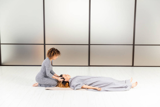 Bienestar concepto saludable. Meditación de dos mujeres en el suelo. Relájese y zen en la habitación blanca. Cuidado corporal
. - Foto, Imagen