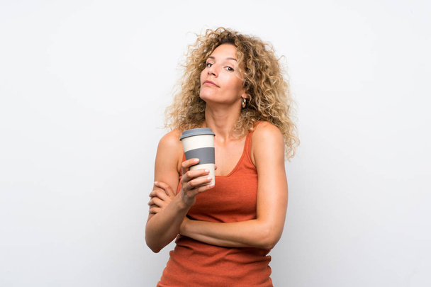 junge blonde Frau mit lockigem Haar hält eine zum Mitnehmen Kaffee kochende Geste, während sie die Schultern hebt - Foto, Bild
