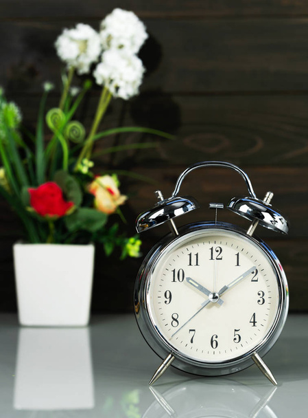 Reloj despertador y florero en la mesa
 - Foto, imagen