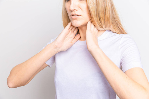 Donna che controlla la ghiandola tiroidea da sola. Primo piano di donna in t-shirt bianca che tocca il collo con macchia rossa. Disturbo tiroideo include gozzo, ipertiroide, ipotiroide, tumore o cancro. Assistenza sanitaria. - Foto, immagini