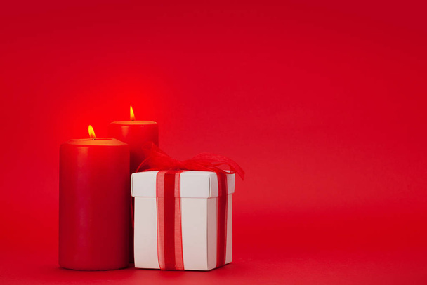 Valentines day greeting card with gift box and burning candles over red background with copy space for your greetings - 写真・画像