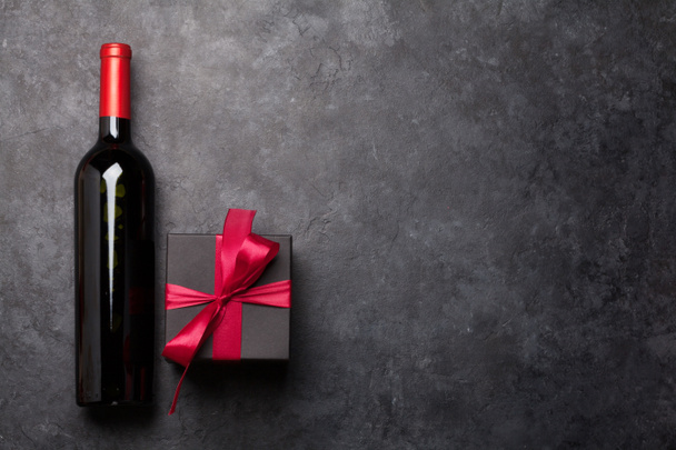 Valentines day greeting card with gift box and red wine bottle on stone background. Top view flat lay with space for your greetings - Photo, Image
