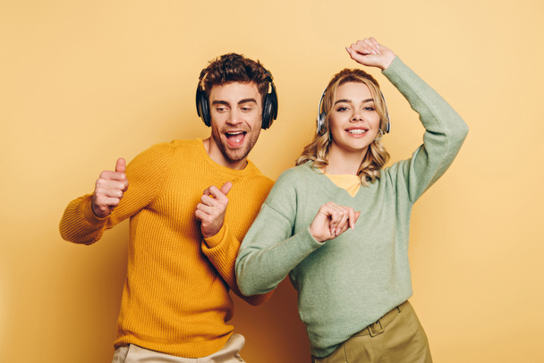 happy couple dancing while listening music in wireless headphones on yellow background - Photo, Image