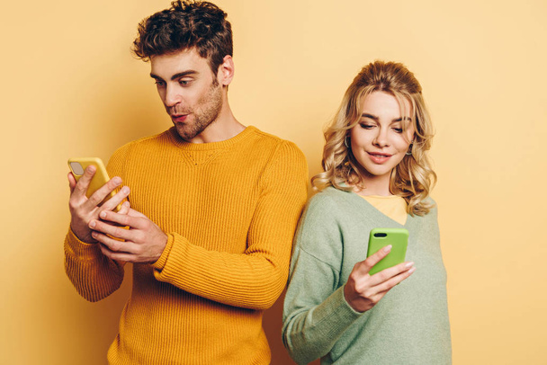 coppia positiva e attenta che chatta su smartphone su sfondo giallo
 - Foto, immagini