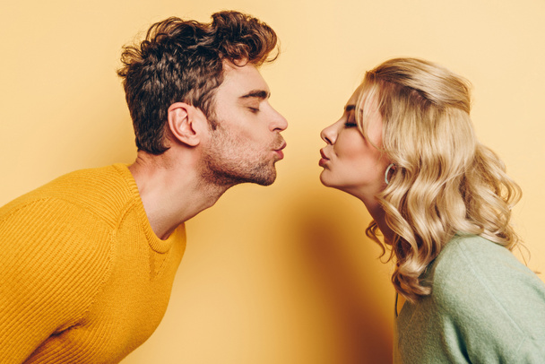 side view of man and woman kissing with closed eyes on yellow background - Foto, Imagem