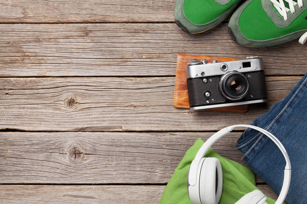 Clothing and accessories. Sneakers, jeans and camera. Urban outfit for everyday or travel vacation on wooden background with copy space. Top view flat lay - Photo, Image
