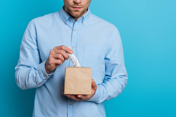 cropped view of upset young man taking paper napkin from pack on blue background - Foto, Bild