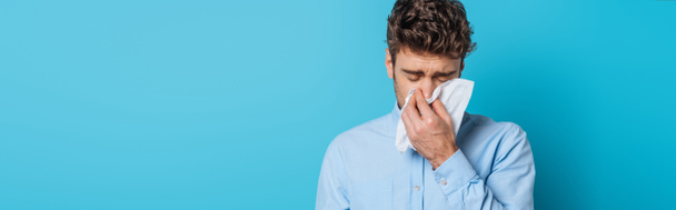 panoramic shot of diseased man sneezing in paper napkin on blue background - Φωτογραφία, εικόνα