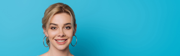 panoramic shot of attractive, cheerful girl smiling at camera on blue background - Foto, imagen