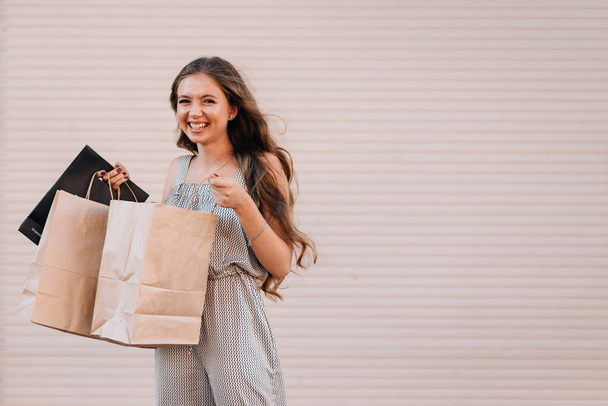 Dziewczyna raduje się z zakupów, śmieje i trzyma papierową torbę otwartą na tle ściany - Zdjęcie, obraz
