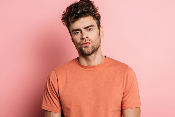 offended young man looking at camera on pink background - Фото, зображення