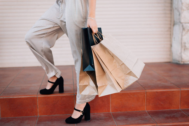 A girl in trousers after shopping stands on the steps with packa - 写真・画像