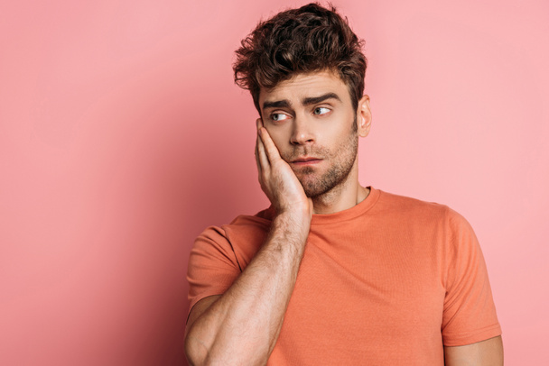 upset young man touching chick while suffering from toothache on pink background - Photo, Image