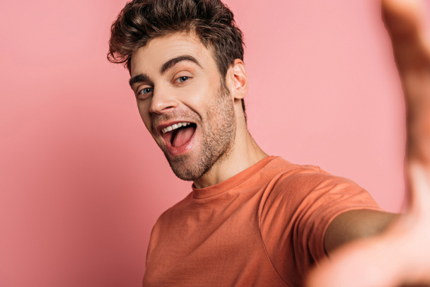 excited man taking selfie while looking at camera on pink background - Photo, Image