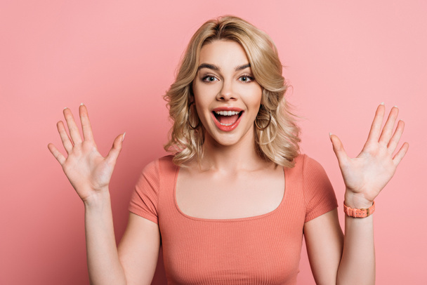 cheerful girl waving hands while smiling at camera on pink background - Photo, Image