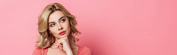 panoramic shot of pensive girl looking away while holding hand near chin on pink background - Zdjęcie, obraz