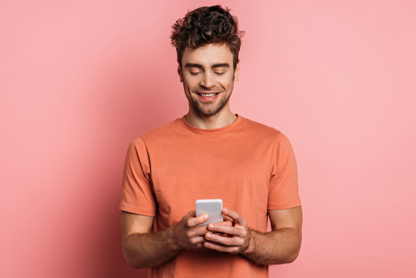 smiling young man chatting on smartphone on pink background - 写真・画像