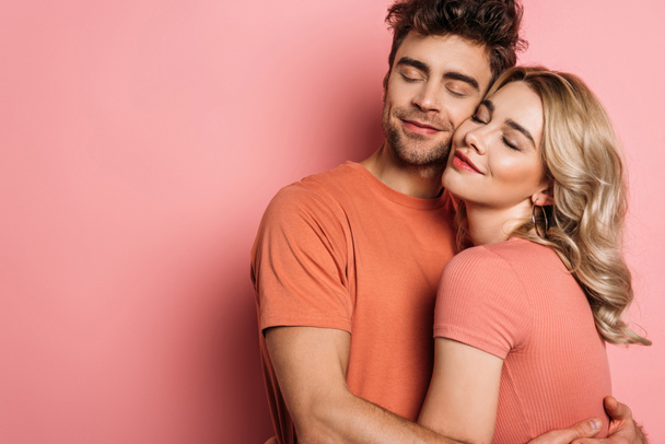 happy young couple embracing with closed eyes on pink background - Фото, зображення