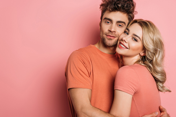 happy young couple embracing while looking at camera on pink background - Photo, image
