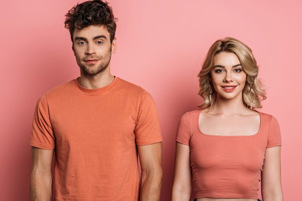 young, positive man and woman looking at camera on pink background - Foto, Bild