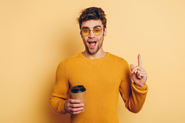 opgewonden man met idee gebaar terwijl het houden van koffie te gaan op gele achtergrond - Foto, afbeelding