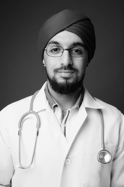 Зйомки молодого бородатого індійського сикхського лікаря проти сірого фону в чорно-білому - Фото, зображення