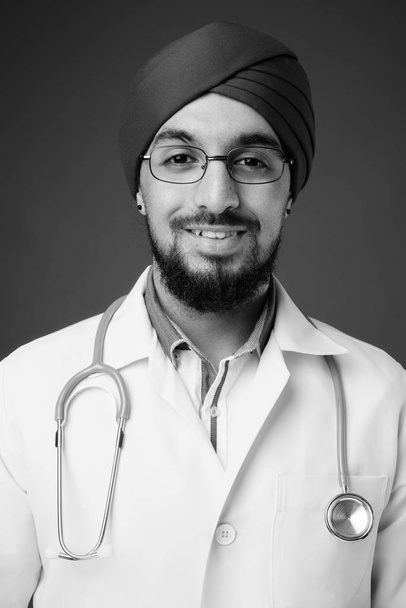 Estudio de joven barbudo indio Sikh hombre médico sobre fondo gris en blanco y negro - Foto, Imagen