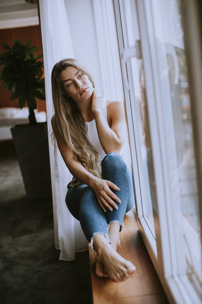 Beautiful young woman sitting by the window in apartment - Foto, afbeelding